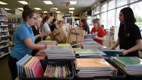 busy retail scene with employees organizing school supplies and stationery in a well-lit store environment featuring colorful notebooks and bags