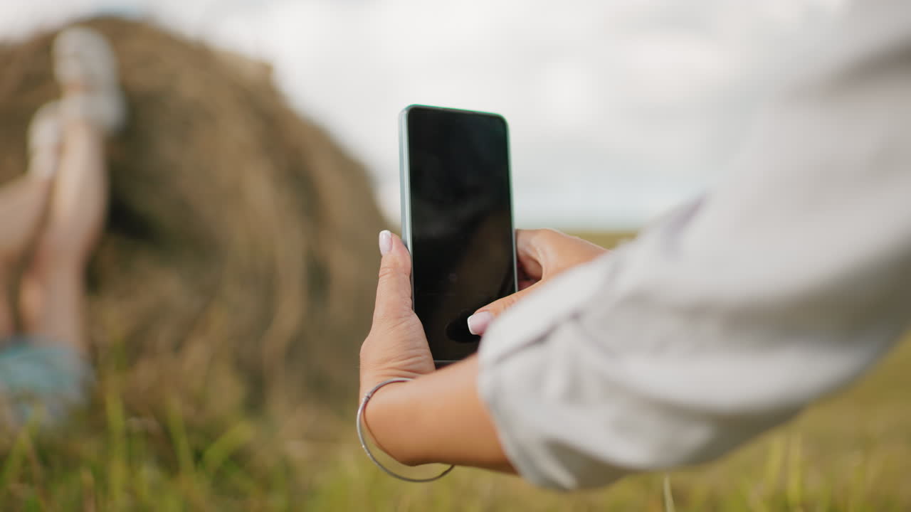 장갑을 입은 여성이 누군가의 다리를 에 놓은 사진을 찍는 클로즈업 드 뷰, 배경은 약간 흐릿하며 시골 풍경의 스마트폰 사진에 초점을 맞추고 있습니다.