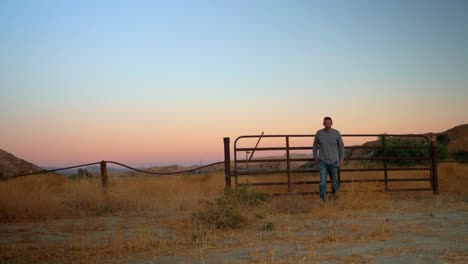 static shot of a man walking from a country gate, on the californian countryside, at dusk, sunny evening