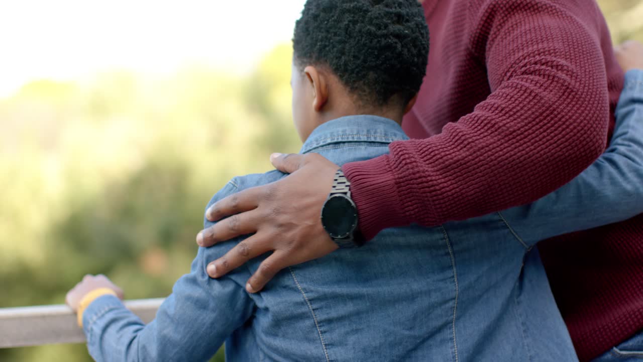 Padre e figlio afroamericani appoggiati alla ringhiera che ammirano il panorama e guidano il bambino con uno smartwatch