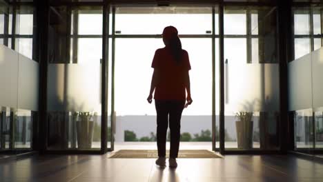 a figure exiting through glass doors at sunset, silhouetted against the light in a modern space, capturing a moment of departure and reflection