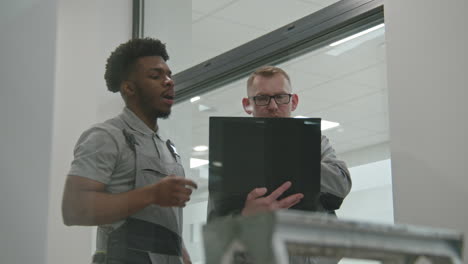 two colleagues collaborating and discussing something on a device in a modern office or workshop setting