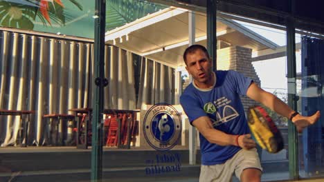 man plays the ball off the back wall in a padel match