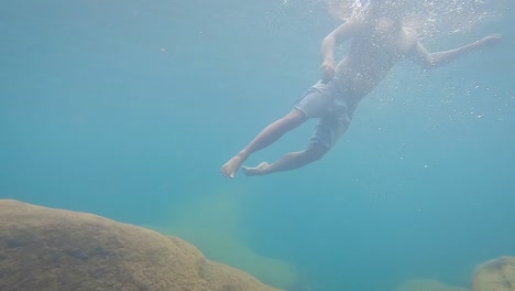 hombre joven nadando bajo el agua en agua azul clara en el día desde un ángulo bajo