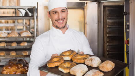 smiling caucasian male baker wearing apron preparing rolls in professional bakery