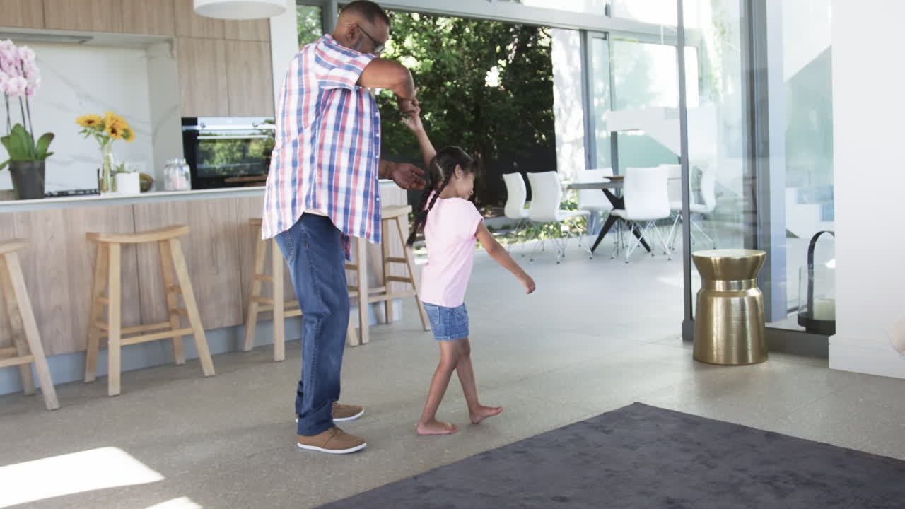 Biracial grandfather teaches a young biracial granddaughter to dance in a modern home