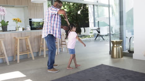 Biracial-grandfather-teaches-a-young-biracial-granddaughter-to-dance-in-a-modern-home