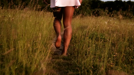 Black-woman-in-skirt-walks-barefoot-through-path-in-field-with-high-grass-during-a-warm-summer-day