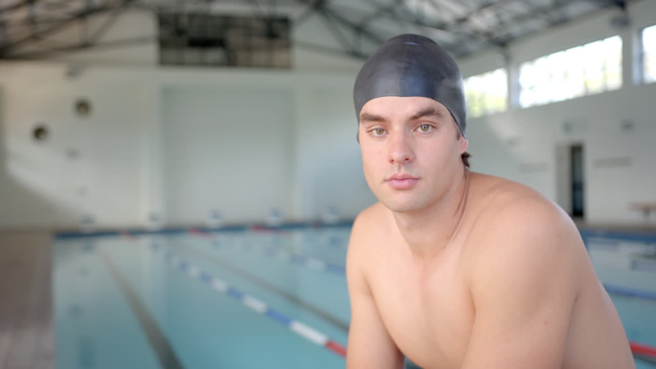 male swimmer wearing swim cap posing by indoor pool, preparing for training session, copy space