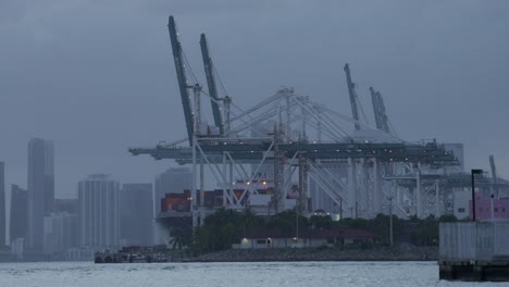 towering shipping cranes stand over cargo containers as twilight settles over the port of miami skyline.