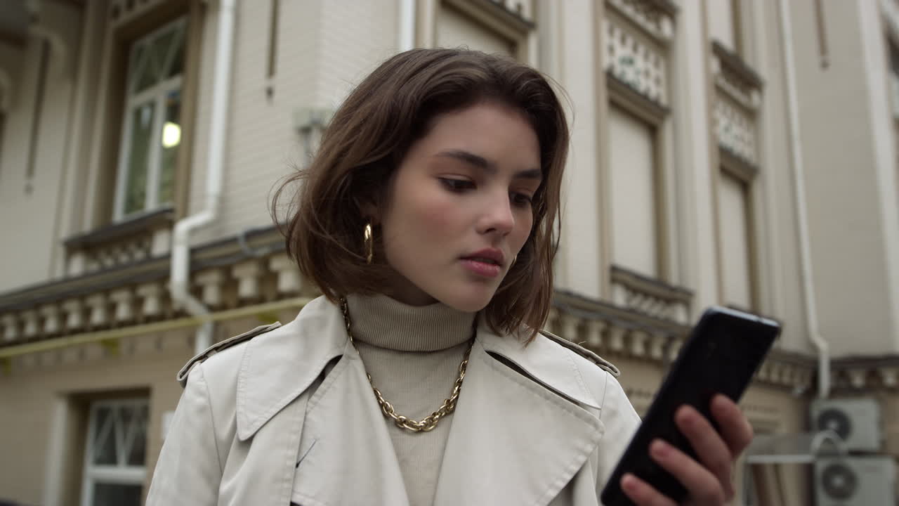 Donna concentrata che telefona per strada in città. Ragazza seria con lo smartphone all'aperto.