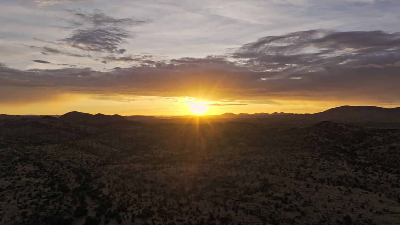 Filmagem de drone de um pôr do sol radiante sobre o deserto da Namíbia, com luz dourada quente banhando o terreno ondulado pontilhado por vegetação esparsa