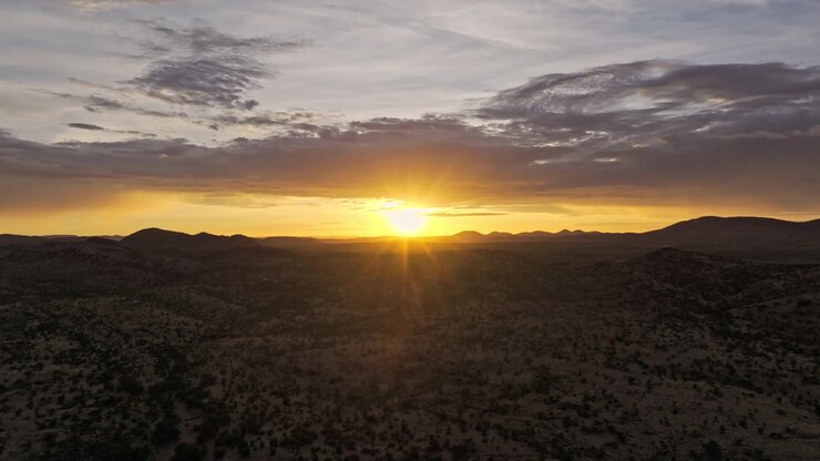 Filmagem de drone de um pôr do sol radiante sobre o deserto da Namíbia, com luz dourada quente banhando o terreno ondulado pontilhado por vegetação esparsa