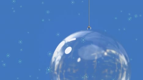 animation of snow falling over glass christmas bauble on blue background