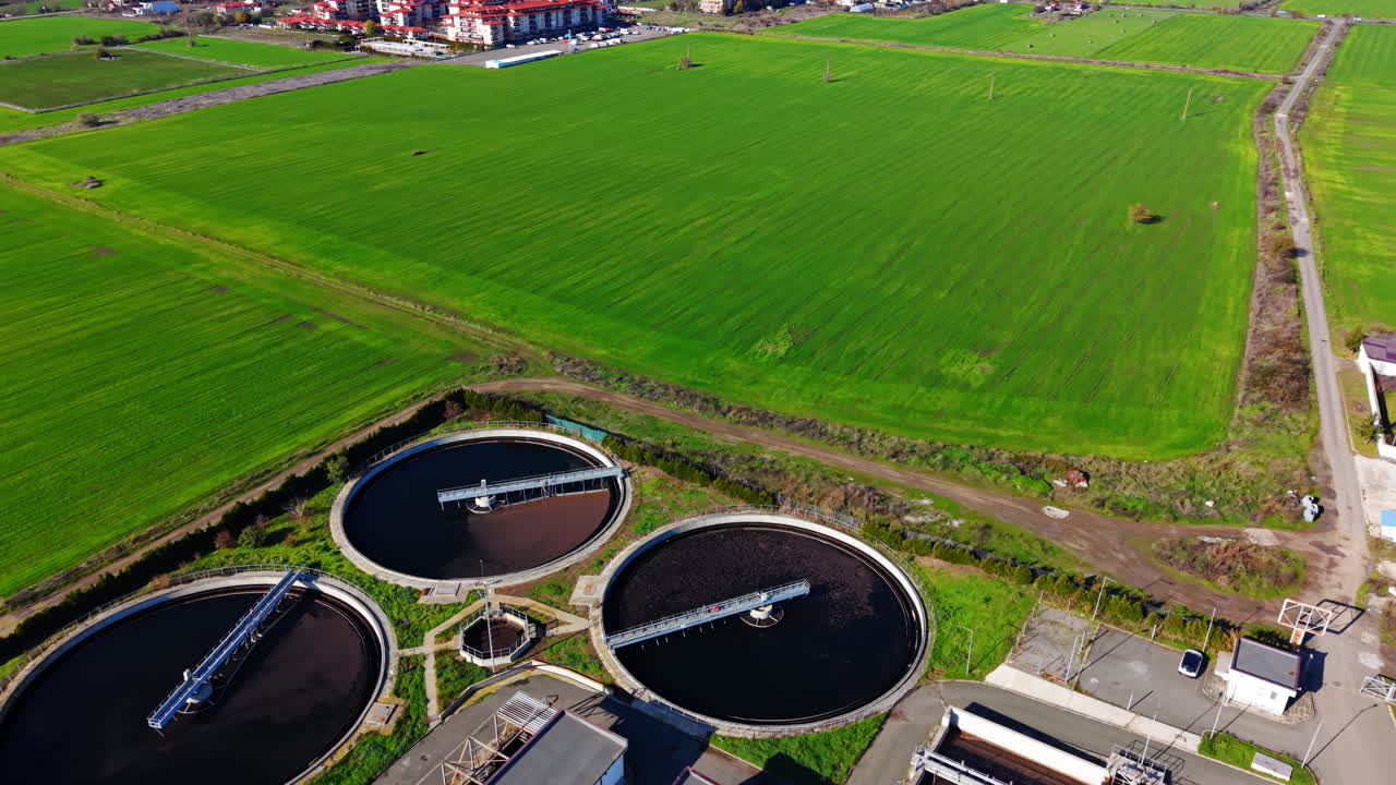 Wide angle drone view of a complete sewage treatment plant surrounded by green agricultural fields near a coastal town
