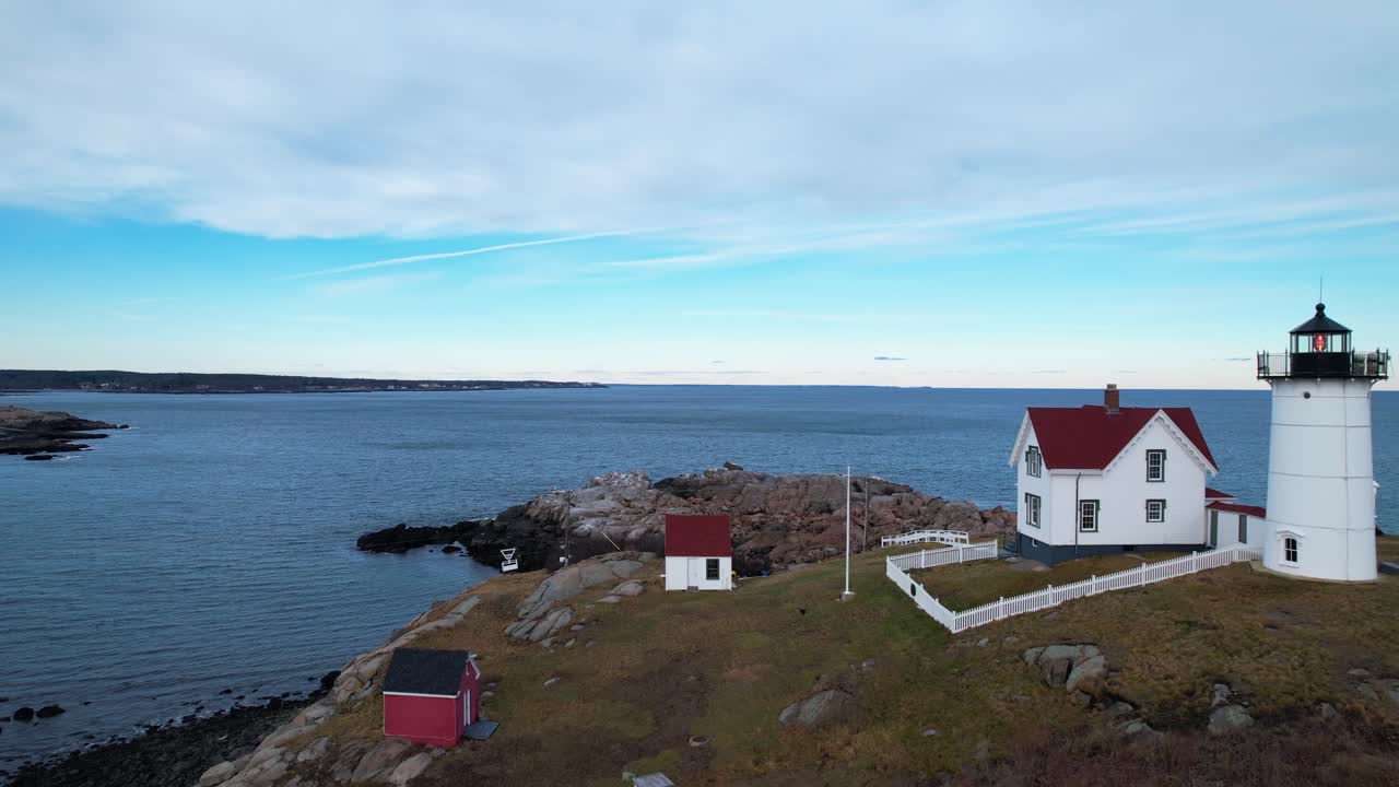Flyover of lighthouse on a rocky coastal island with rippling water and blue sky above
