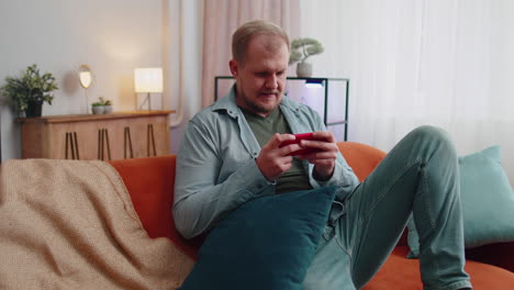 Worried-funny-adult-man-playing-shooter-online-video-games-celebrate-win-on-mobile-phone-at-home