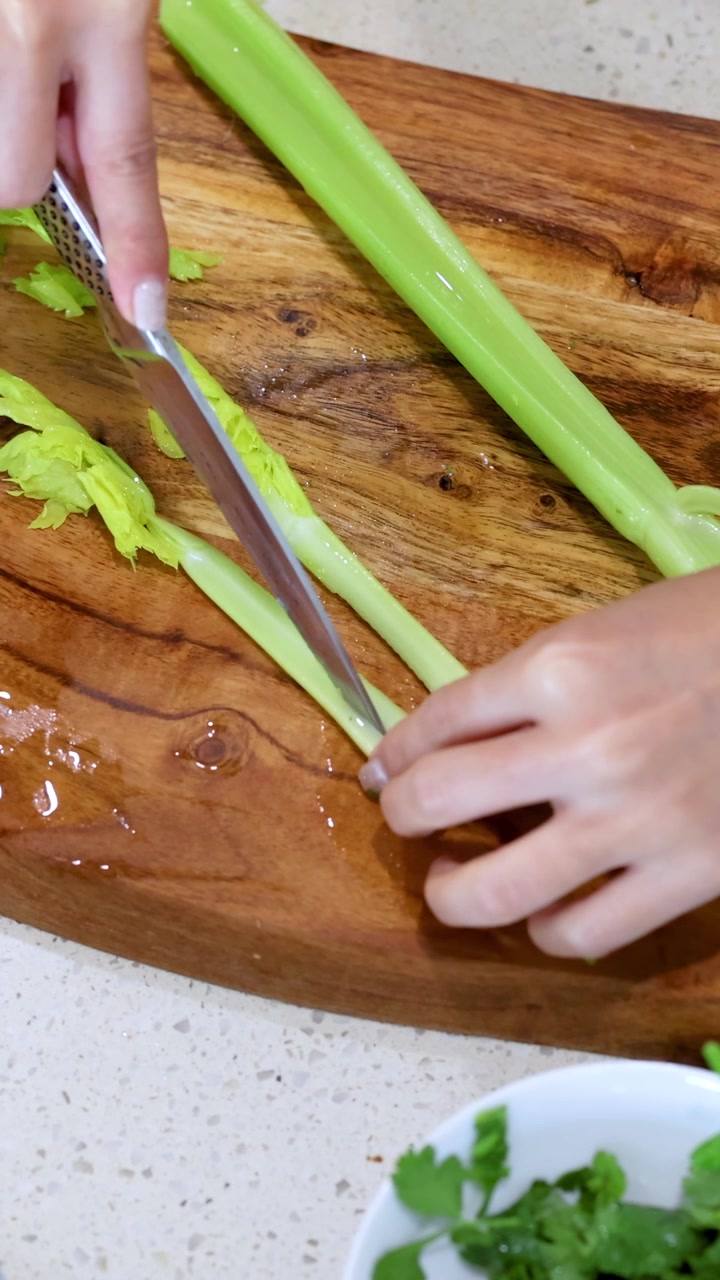 Mani che affettano il sedano su un tagliere di legno in un ambiente cucina luminoso. Primo piano con illuminazione naturale.