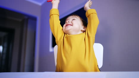 baby boy drawing with red pen. lovely toddler raises hands rejoicing cheerfully. close up.