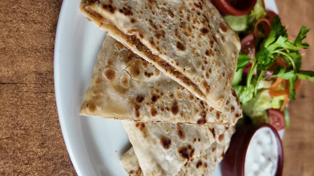 Stacked flatbreads with filling, served with a side salad and dipping sauce