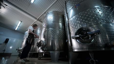 a happy successful farmer or winemaker is walking in the middle of wine tanks and checking a fermentation grade of high quality wine production in a modern winemaking facility or winery.