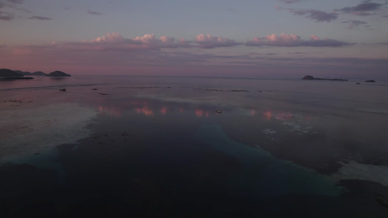 Pink Purple Sunset Over the Sea Near Komodo Island with Colorful Clouds Reflecting in Shallow Calm Water - Aerial Side Dolly