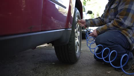 a man fills up the air tires of their red car with a blue tube