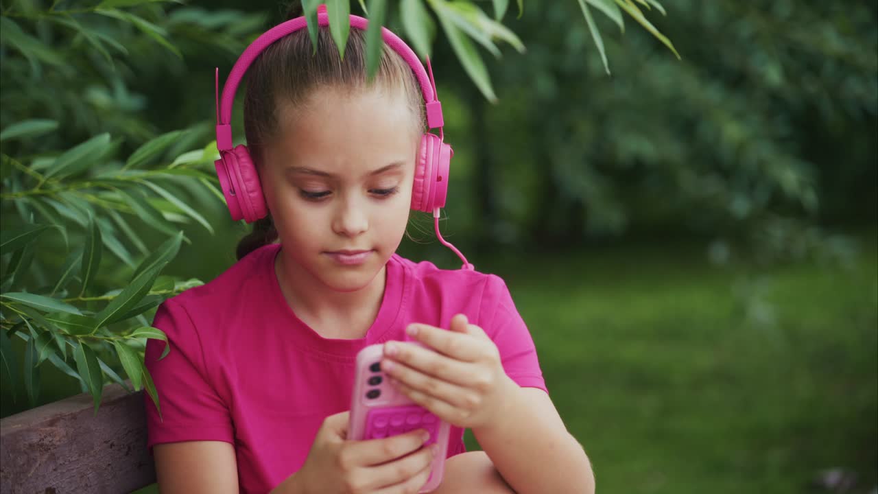 A Young Girl Enjoys Her Music with Vibrant Pink Headphones While Relaxing in Nature, Capturing the Essence of Leisure and Creativity