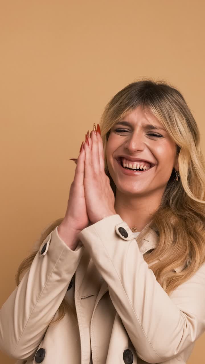 Cheerful transgender woman in trench coat laughing against beige background