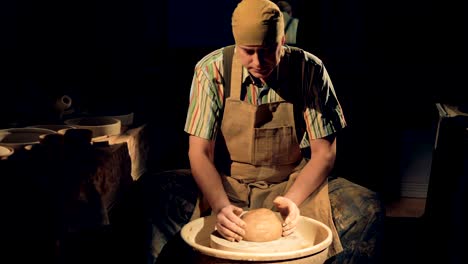 a potter presses a large clay ball onto a pottery wheel.