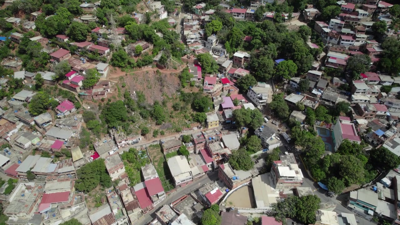 Droneopptak som vipper opp og avslører et vidstrakt, enkelt boligområde bygget inn i en bratt dalside i La Guaira, med utsikt over Venezuelas kystlinje