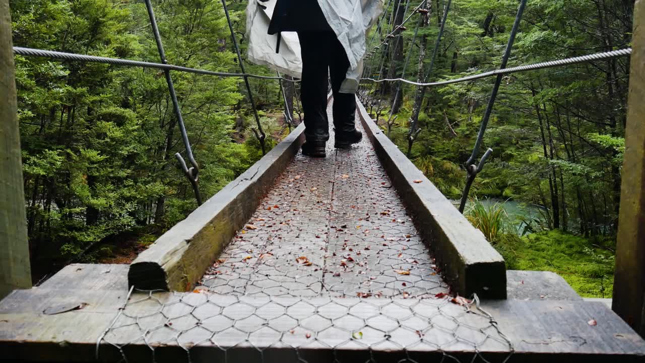 hiker wearing rain poncho crosses footbridge in forest