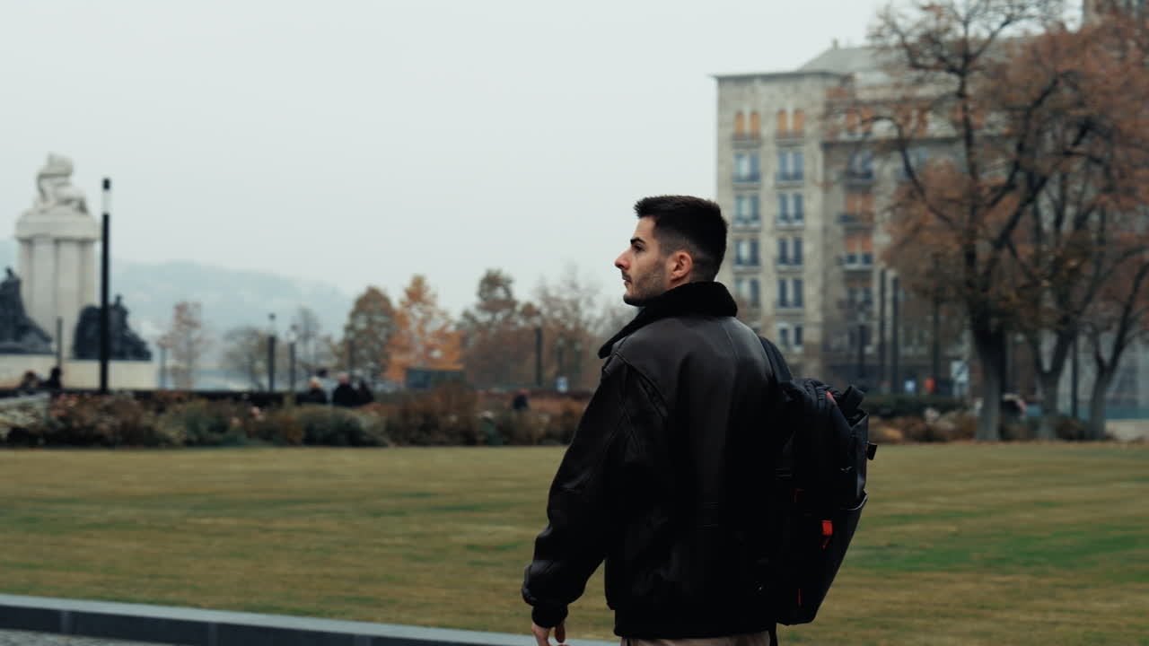 A young traveler with a backpack walks through a peaceful park near the Budapest Parliament. Calm moment surrounded by greenery and iconic architecture