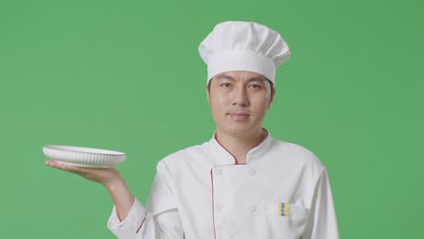 el chef asiático sostiene un plato mientras camina en el estudio de fondo de la pantalla verde