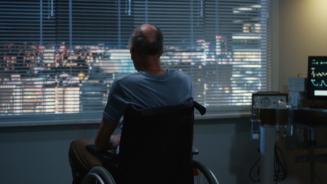Elderly Man in Wheelchair Looking Out Hospital Window at Night
