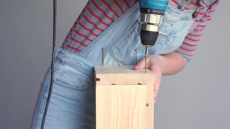 una mujer hace un trabajo no femenino - perfora un agujero con un destornillador en una caja de madera