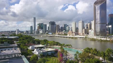 Die-Drohne-Steigt-Unter-Palmen-Herab-Und-Verbirgt-Den-Blick-Auf-Die-Skyline-Und-Den-Fluss-Von-Brisbane,-Australien