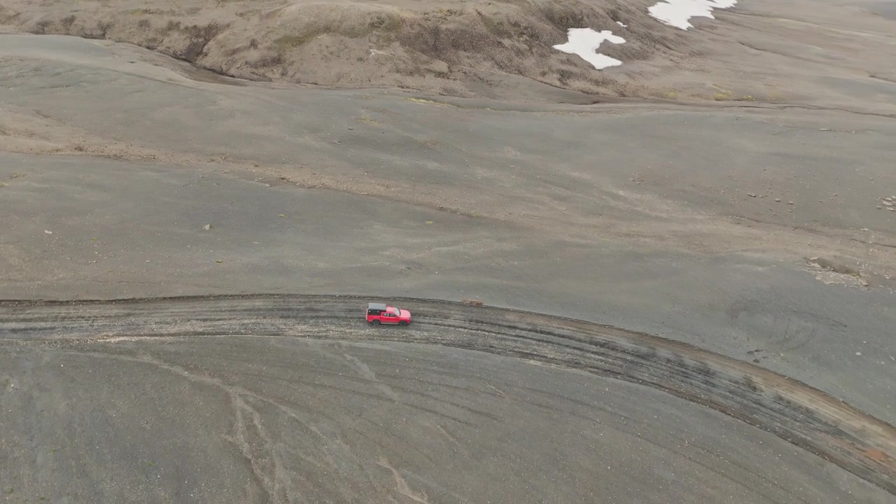 Droneoptagelse fra høj vinkel af en rød SUV, der navigerer i det barske vulkanske landskab i det islandske højland nær Blahylur og Strutur-krateret
