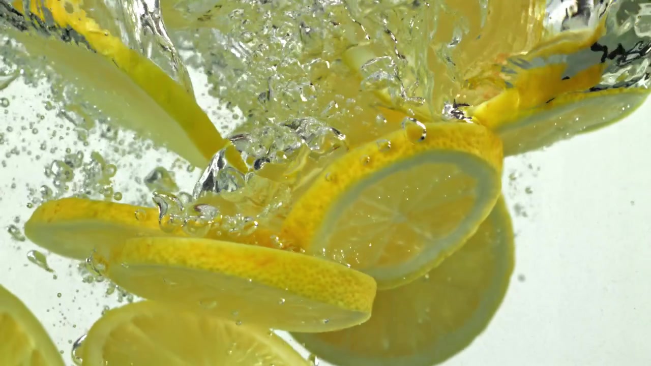 Fresh Lemon Slices Falling into Clear Water with Bubbles