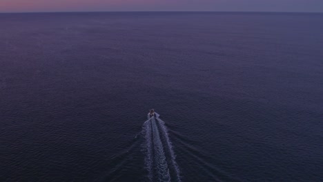 Rising-up-above-speedboat-thats-floating-on-atlantic-ocean-with-colourful-sky,-aerial