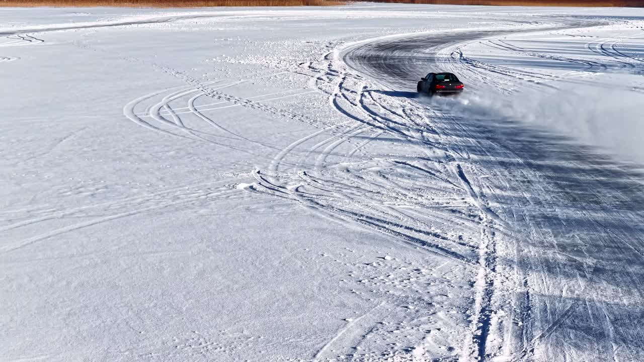 Luftfoto i slow motion, der følger en drifting-bil, der danner buede mønstre i et stort hvidt snefelt.