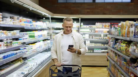 a happy middle-aged shot visitor walks along the shelves with goods and smiles while looking at the phone. the concept of happy