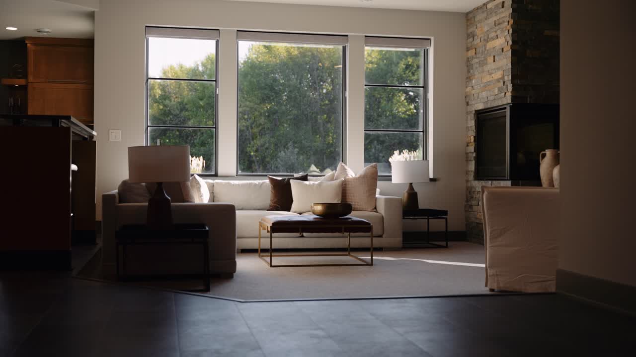 A cozy living room with large windows letting in natural light, a white sofa, and a stone fireplace