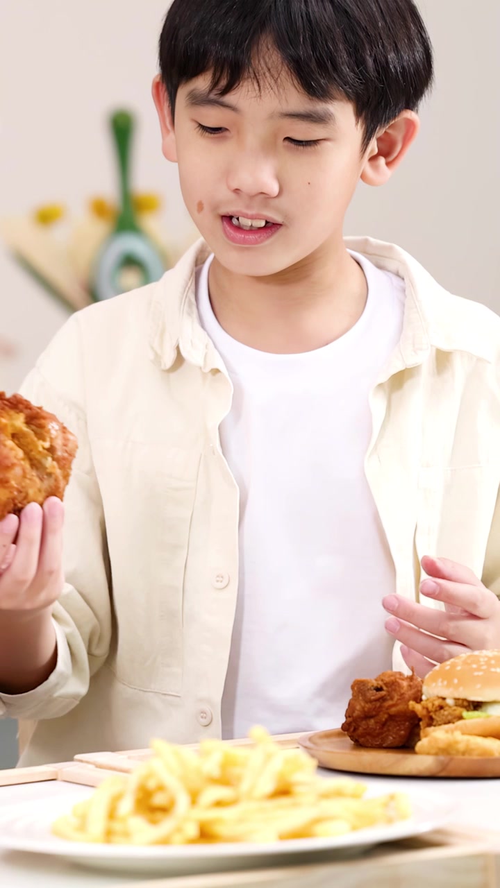 Anak laki-laki tersenyum menikmati ayam goreng dan kentang goreng di meja dalam suasana dalam ruangan yang cerah