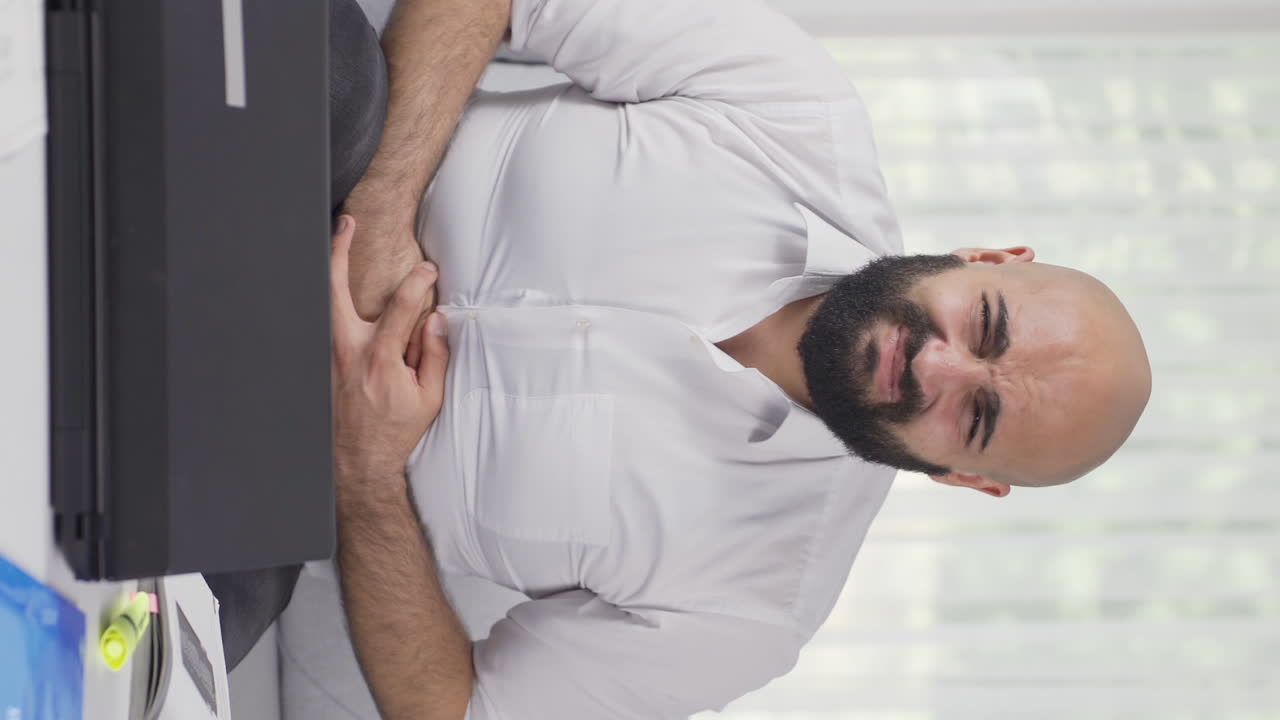 Vertical video of Home office worker man has stomachache.