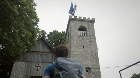 camera tracking from behind a young hiker walkig towards the tower where two flags flutter in the wind