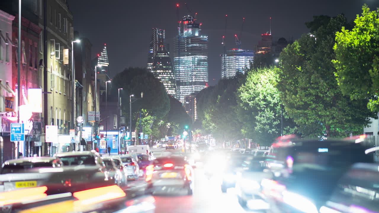 Night time lapse of a busy road in London, UK with cars and buses zooming past and skyscrapers skyline in the background