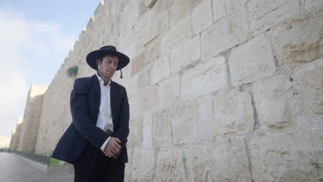 a man in traditional attire stands solemnly against the ancient stone walls of jerusalem, capturing a moment of deep reflection and cultural reverence