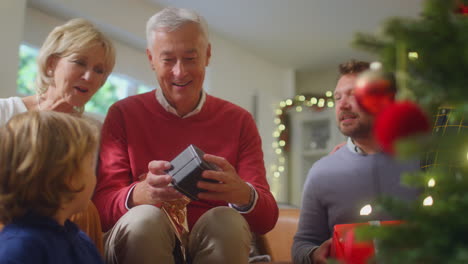 granddaughter handing out presents to multi-generation family around christmas tree at home