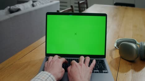 person typing on laptop with green screen